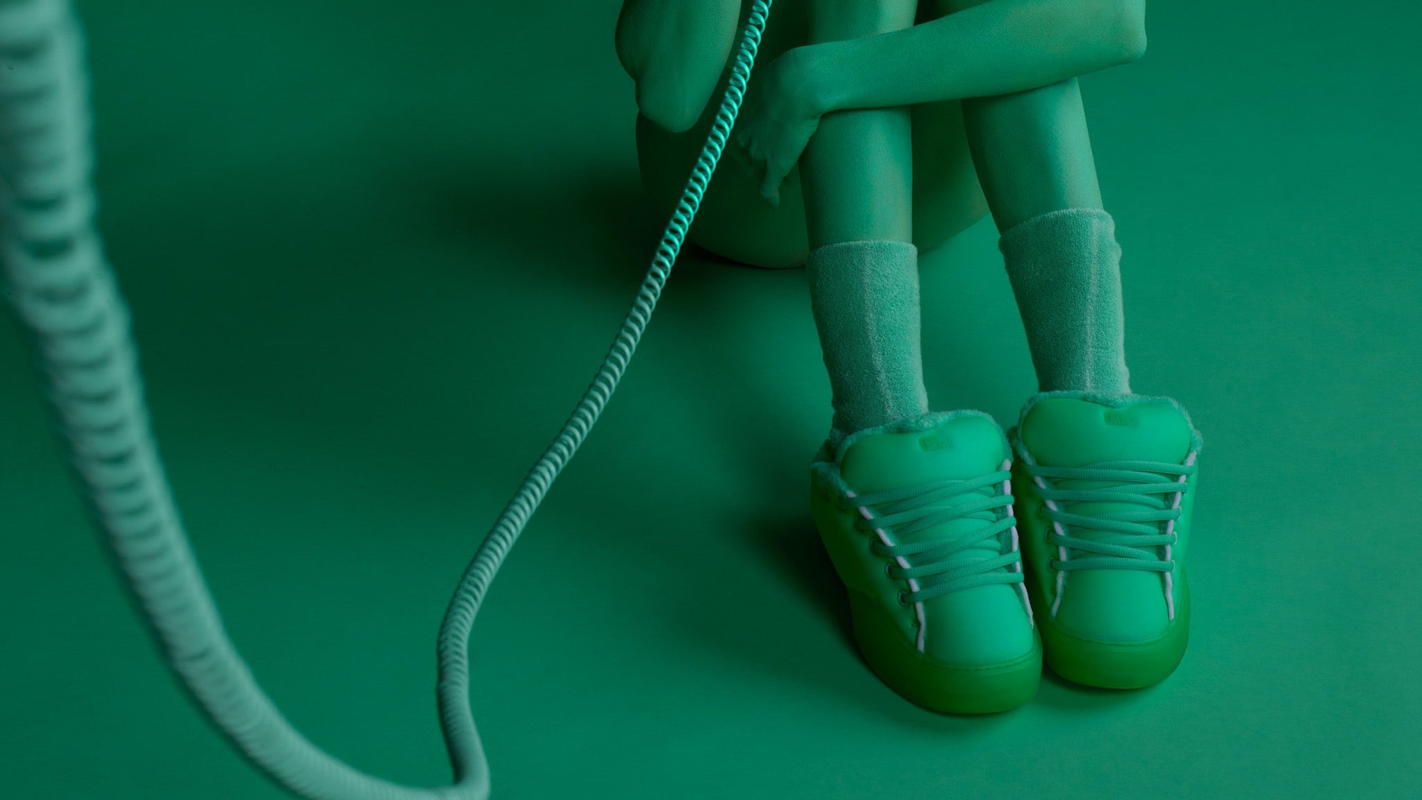 Person sitting on a green surface with a green phone, wearing green shoes and a green outfit.