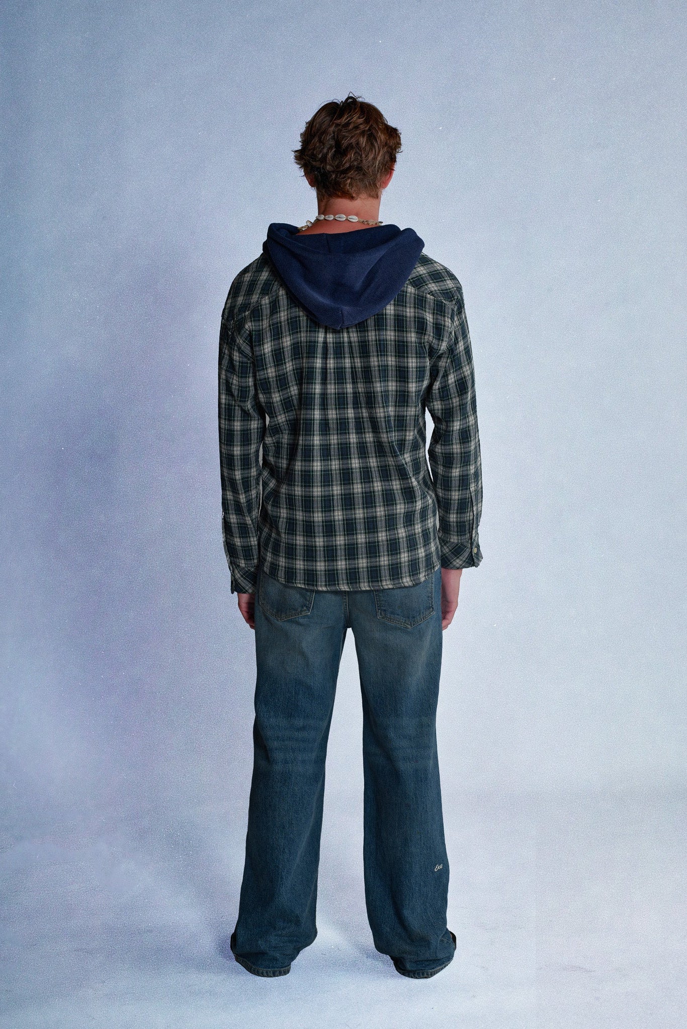 Person wearing a plaid shirt and jeans standing against a plain background