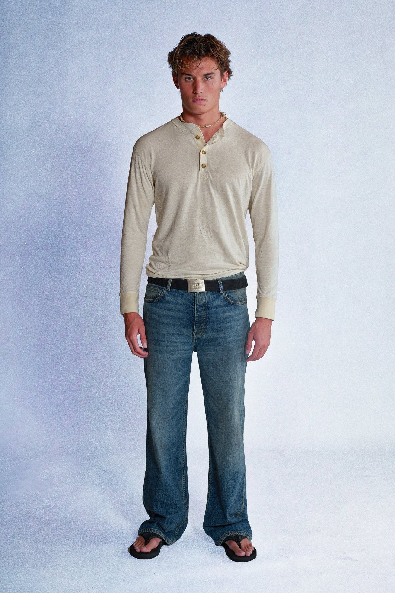 Man wearing a beige long-sleeve shirt and blue jeans against a plain background